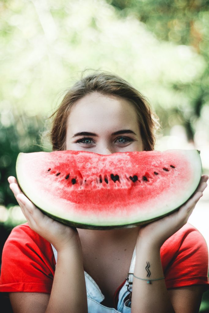 person with watermelon slice in front of her face 